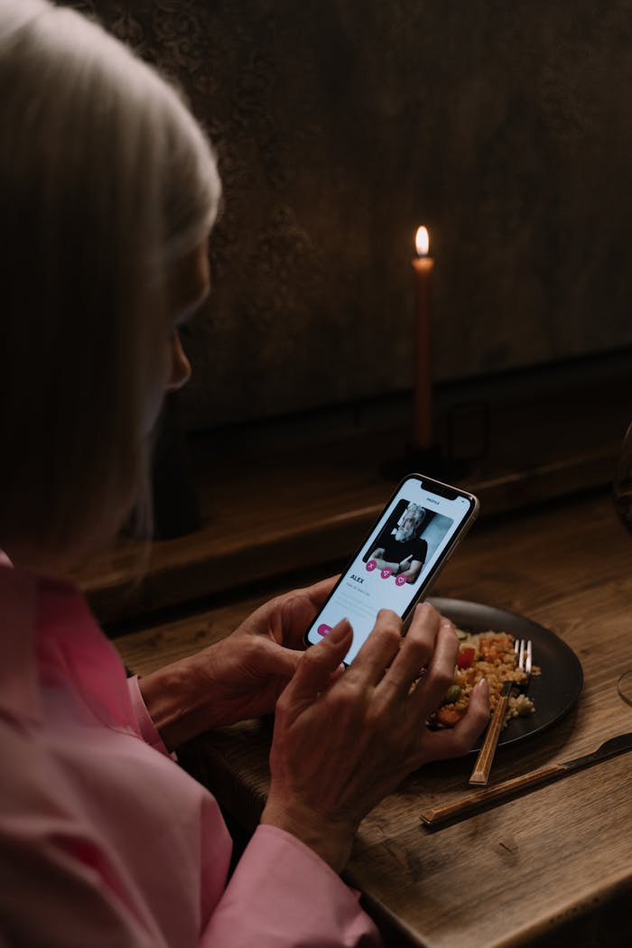 Elderly woman using dating app on smartphone, dining table.